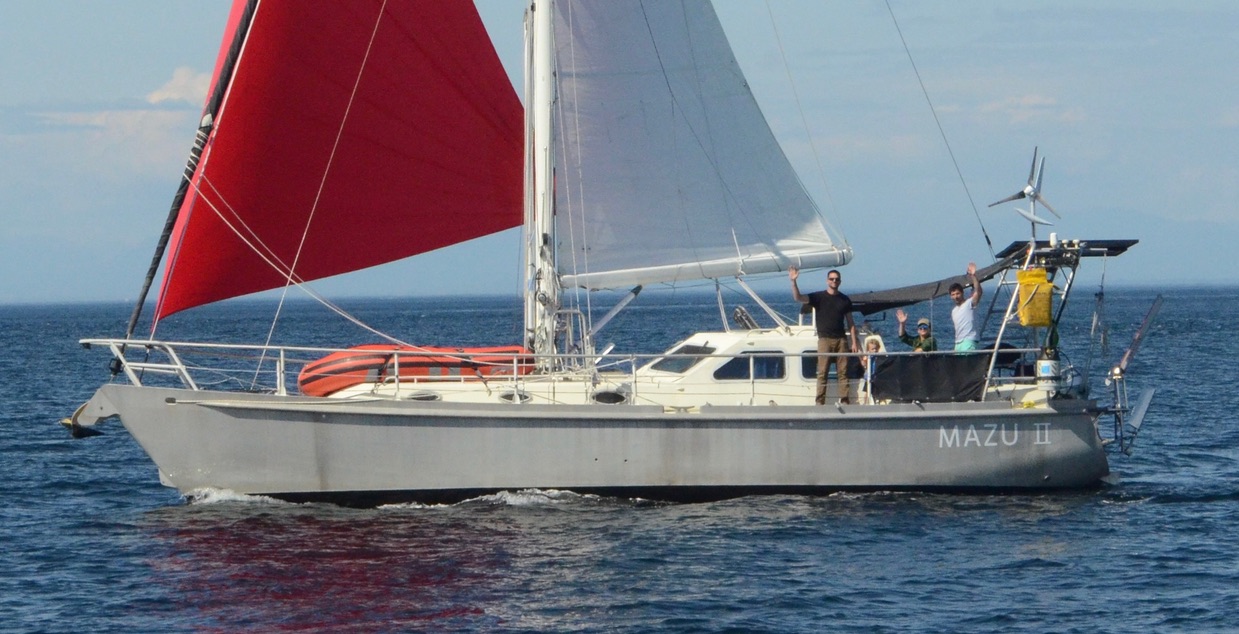 Mazu II underway with red spinnaker, crew waving from the deck